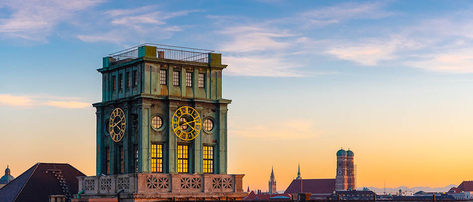 im Vordergrund ist der historische Uhrenturm der TUM zu sehen, im Hintergrund die Frauenkirche - in Abendstimmung